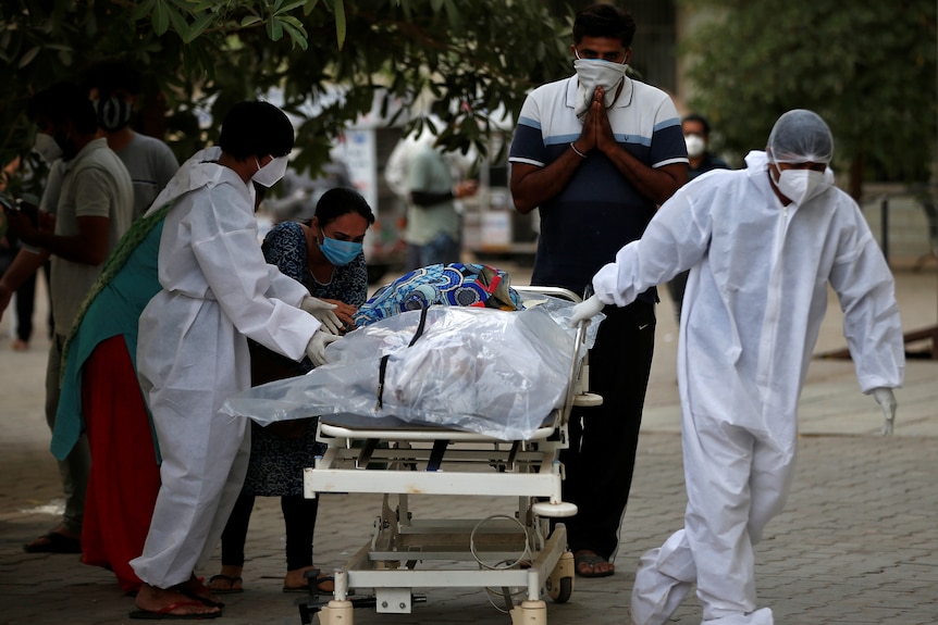 Workers transport a body on a stretcher as family members cry