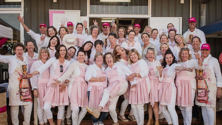 A group of women and men wearing pink aprons poses for a group photo.