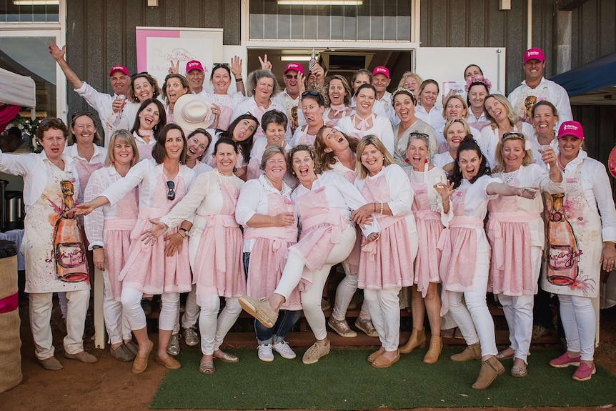 A group of women and men wearing pink aprons poses for a group photo.