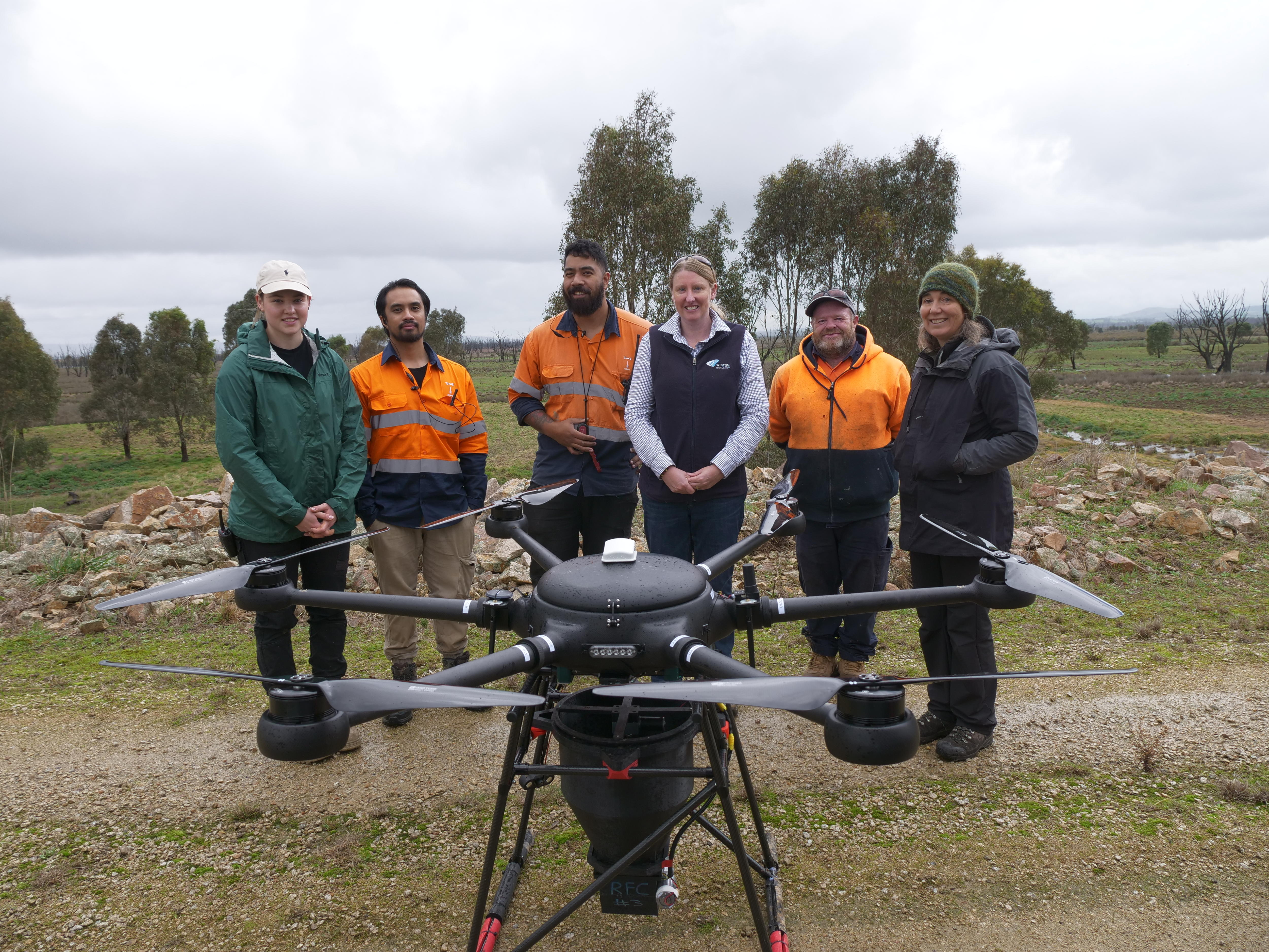 A group of people standing in front of a wetlands area with a drone in front of them 