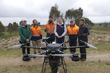 A group of people standing in front of a wetlands area with a drone in front of them 