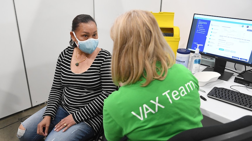 A women sitting down next to a nurse waits for her COVID vaccine shot