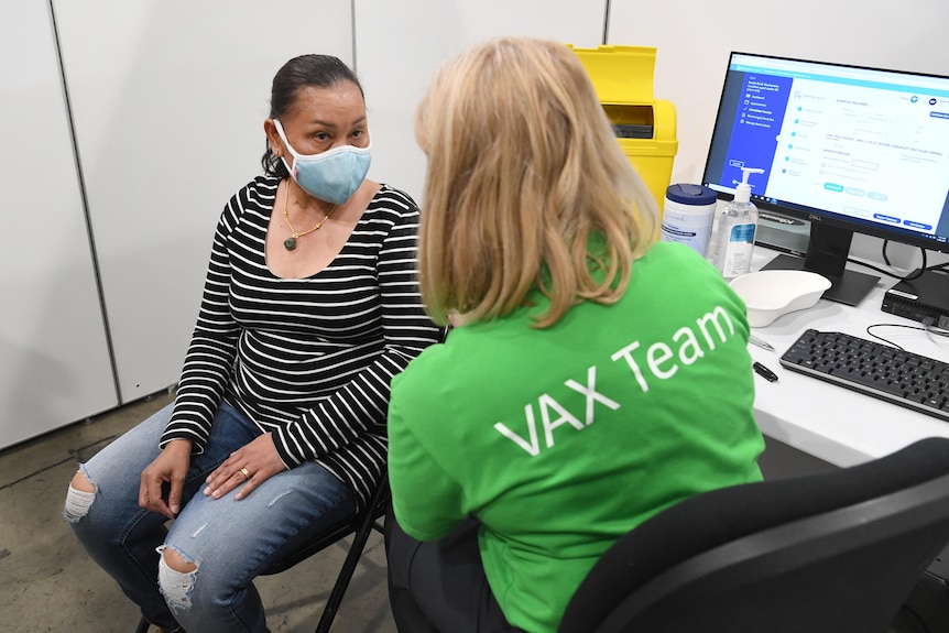 A woman sitting next to a nurse waits for her COVID vaccination