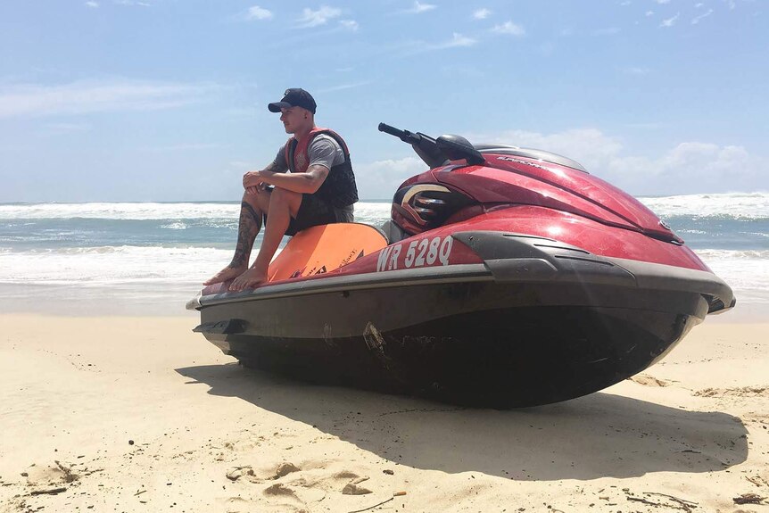 A man with a lifejacket on sits on his red jet ski on the closed Burleigh Beach on Queensland's Gold Coast.