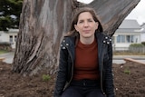 a woman in a black jacket sits in front of a huge tree trunk