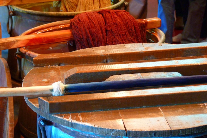 Three vats of dye with yellow, red and blue wool draining above them.