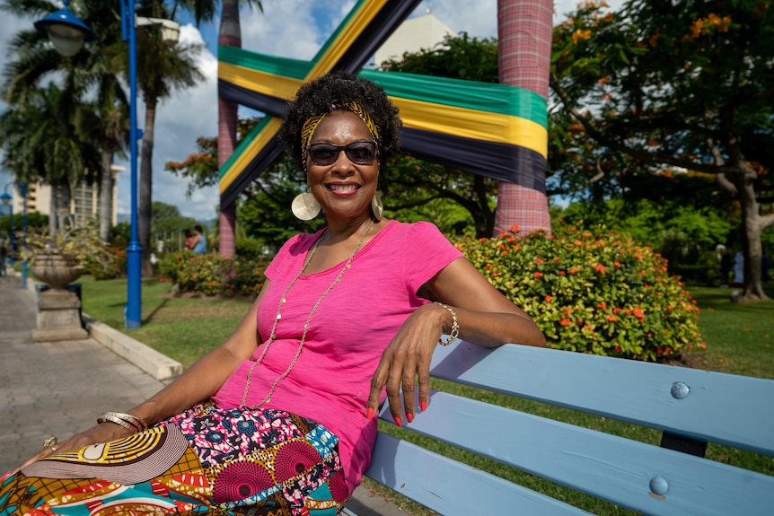 A woman in a vibrant skirt and pink top sits on a park bench 
