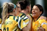 A number of Matildas players embrace and smile in celebration.