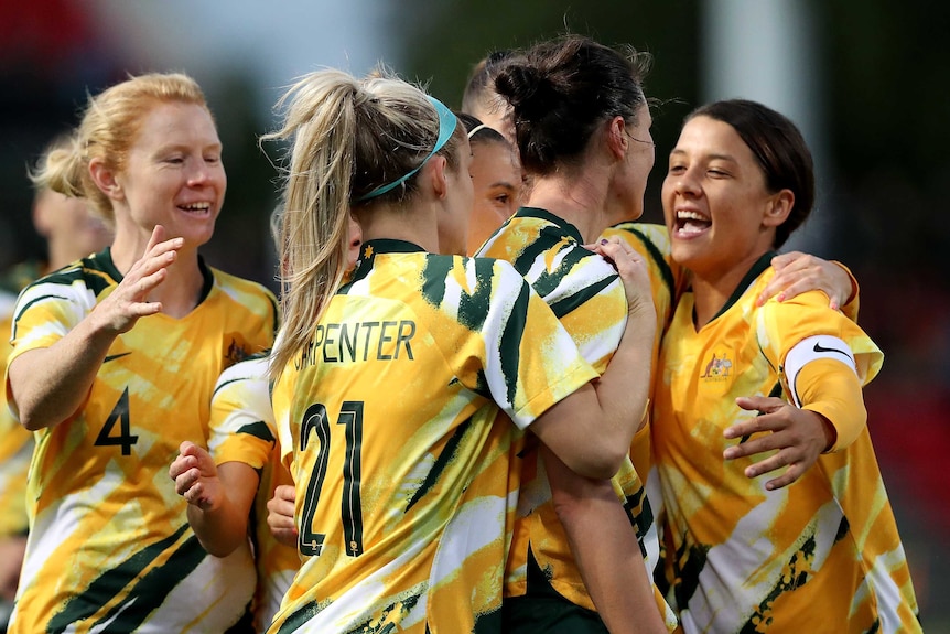A number of Matildas players embrace and smile in celebration.