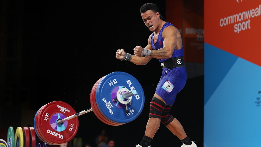 A weightlifter screams in joy as the weights fall to the ground.