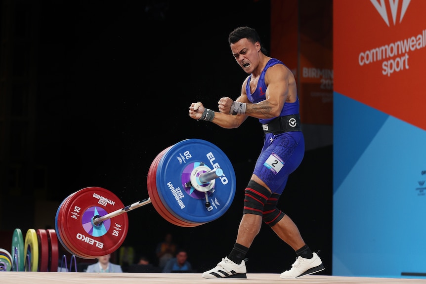 A weightlifter screams in joy as the weights fall to the ground.