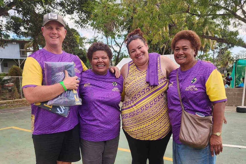 Two Australians and two Fijians wearing purple huddle together on a netball court