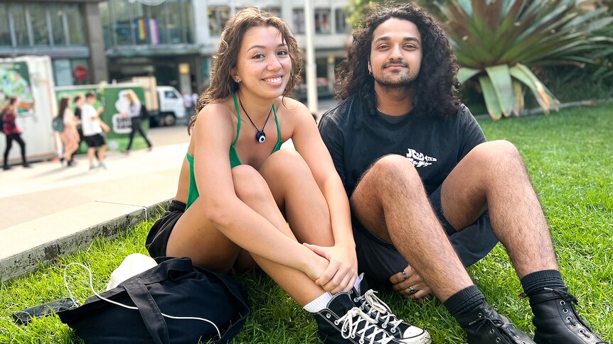 Jaz and Adi smile on a patch of grass at a university campus.