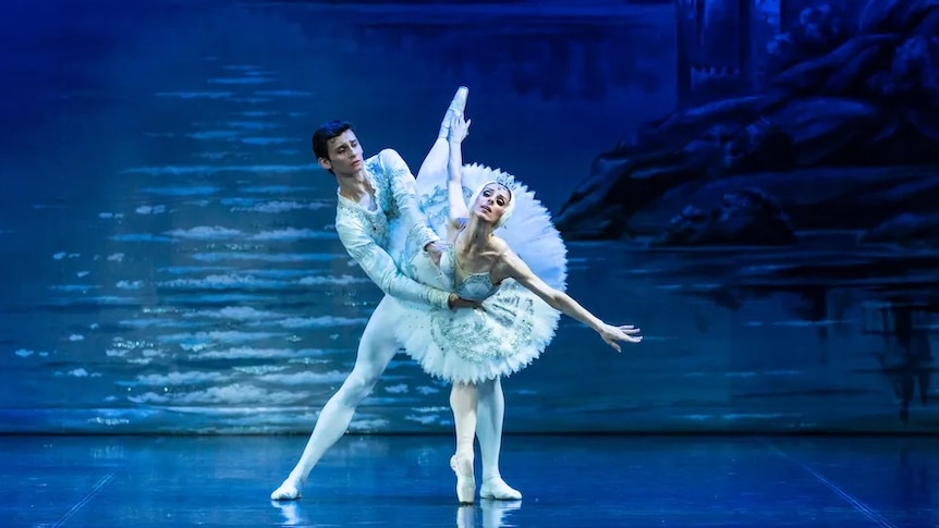 Two ballet performers stand on stage, performing Swan Lake
