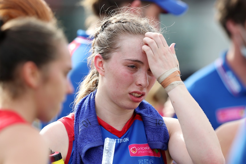 A tired and heat-affected AFLW player puts her hand to her forehead as she wears an ice towel around her neck.