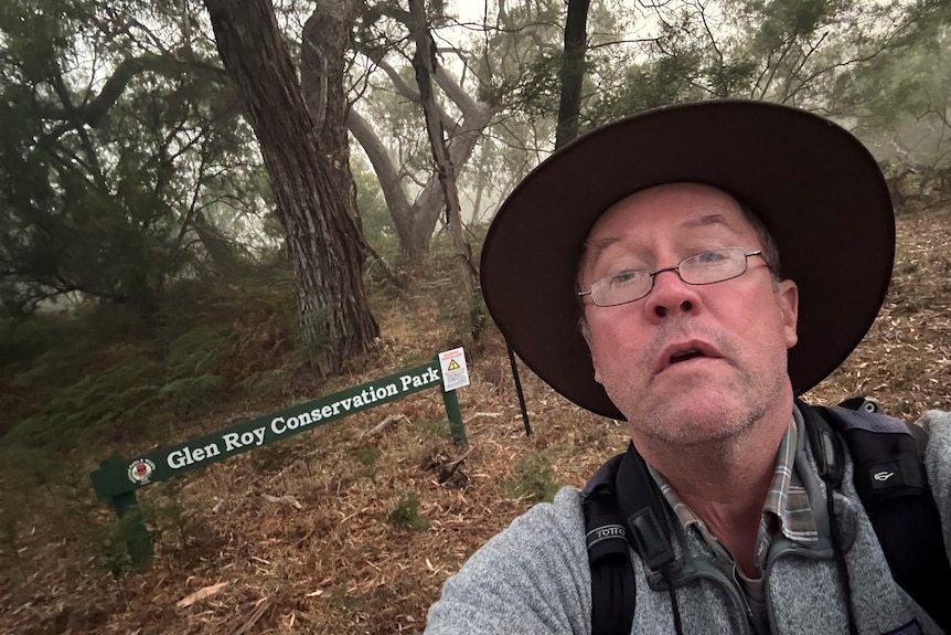 A selfie of a middle-aged man wearing a broad brimmed hat and glasses in a native bush area.