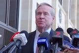 A mid shot of Colin Barnett speaking with a row of microphones under his face.