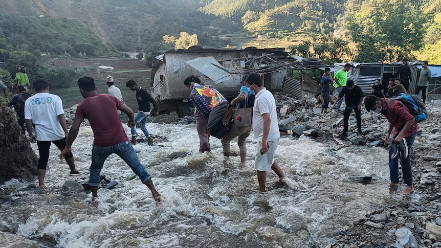 People wade through a flooded area to a damaged house as landslides hit.