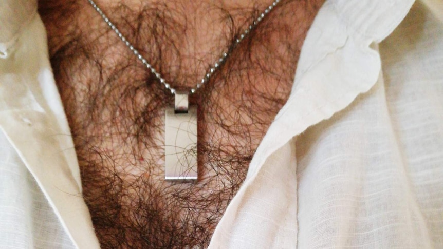 A person wearing a white top, exposing their chest hair and a silver pendant.