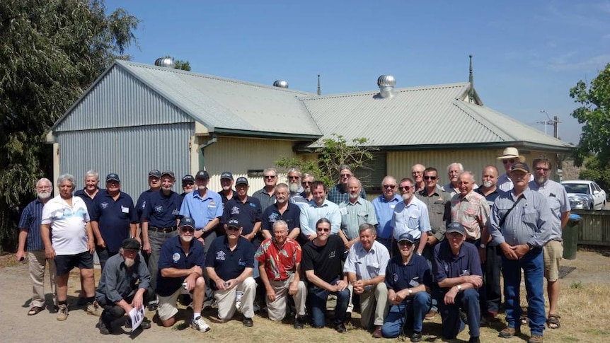 A large group of men pose with Barry Golding in front of the community shed in Goolwa, South Australia.