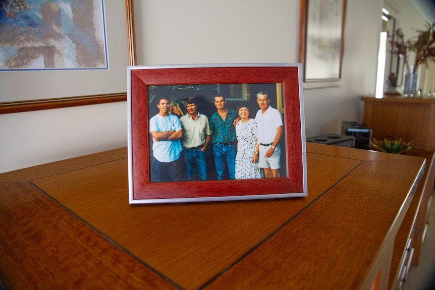A photo frame containing a portrait of a woman with her three sons and her late husband