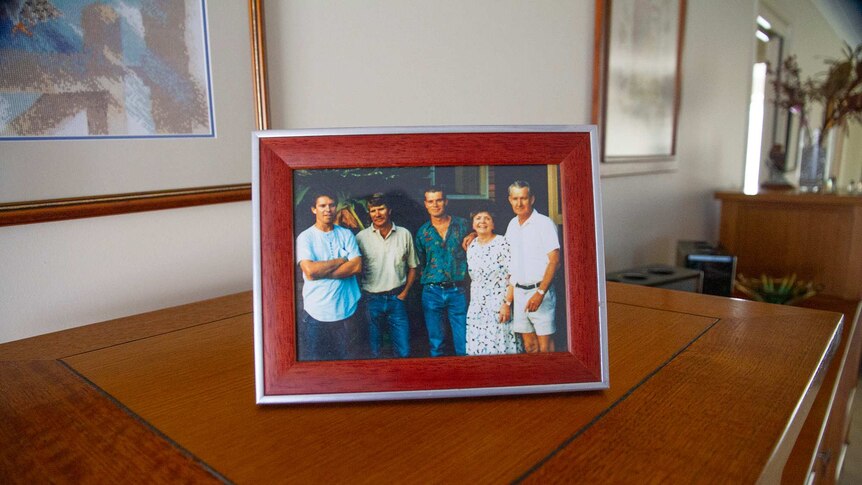 A photo frame containing a portrait of a woman with her three sons and her late husband