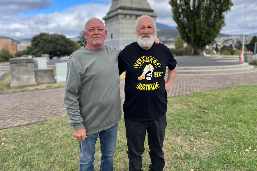 Michael Reardon and Peter Taylor stand with their arms around each other's shoulders in front of the Hobart Cenotaph