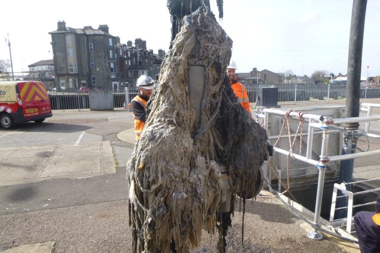 Two workers in high-visibility gear with a huge grey wad of wet wipes