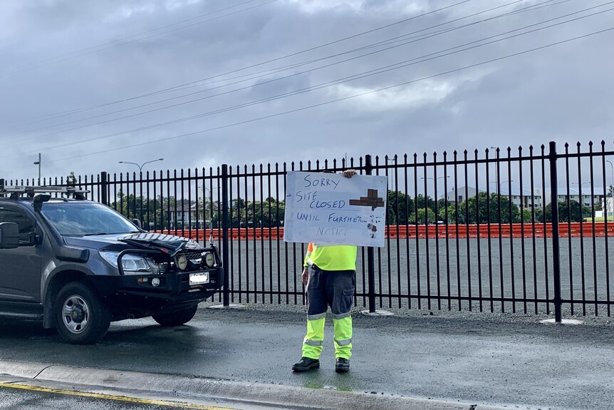 Man holds handwritten 'site closed until further notice' sign at COVID-19 testing site at Robina on the Gold Coast as car waits
