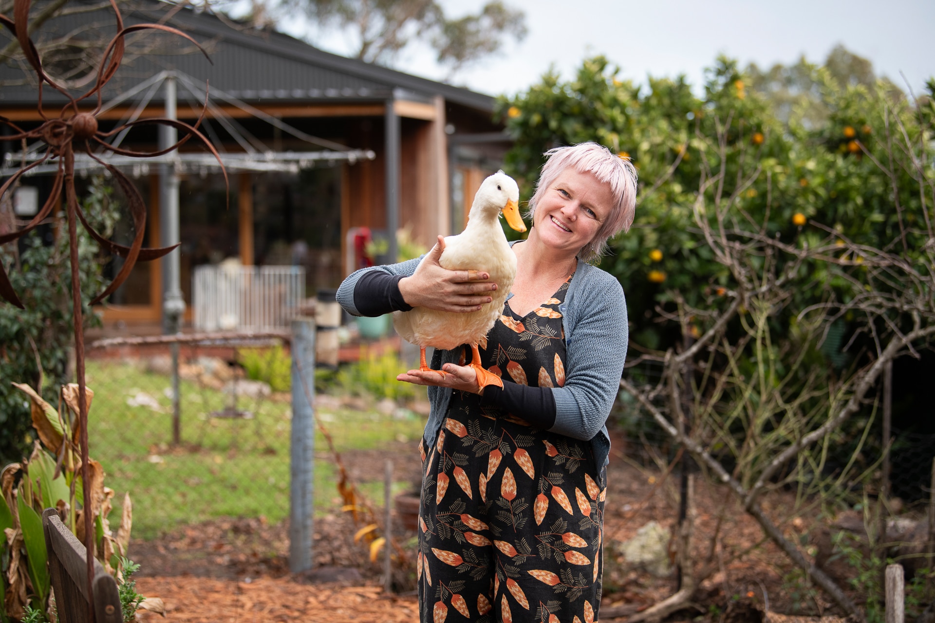 Clare James, holding a duck, stands in a garden. Behind her is a Hills hoist and a house.