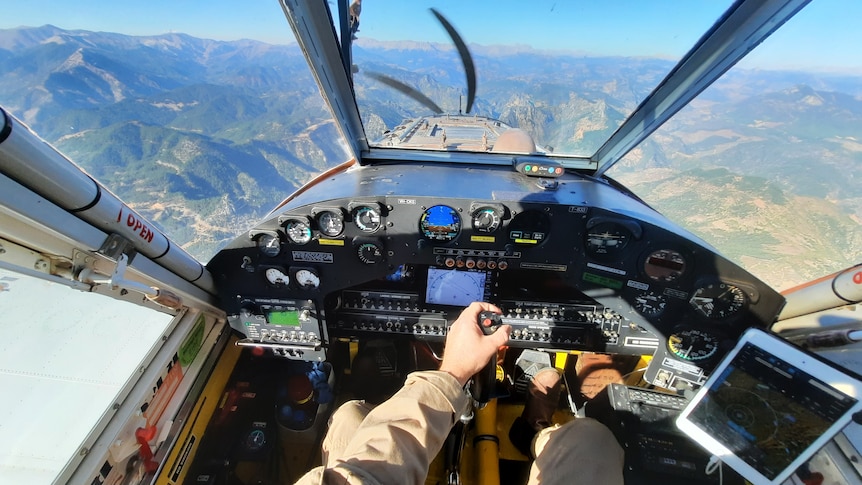 Pilot's view of the cockpit in plane, looking out at mountainous landscape, instruments on dash