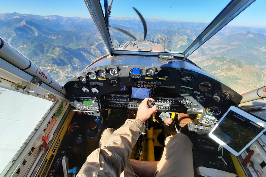 Pilot's view of the cockpit in plane, looking out at mountainous landscape, instruments on dash