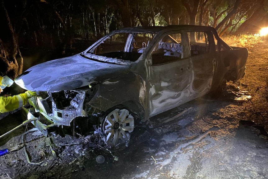 A close-up shot of a burnt-out ute on a dirt road at night.