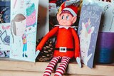 A toy elf sitting on a shelf full of cards and other items.