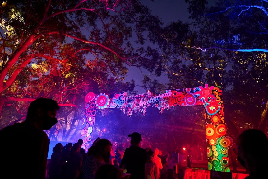 A colourful entrance sign for the Noongar Wonderland, lit at night with people in the foregound