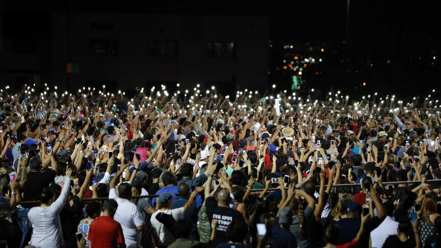 Hundreds of people raise their arms together at a vigil for victims