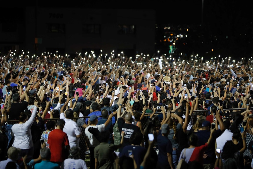 Hundreds of people raise their arms together at a vigil for victims