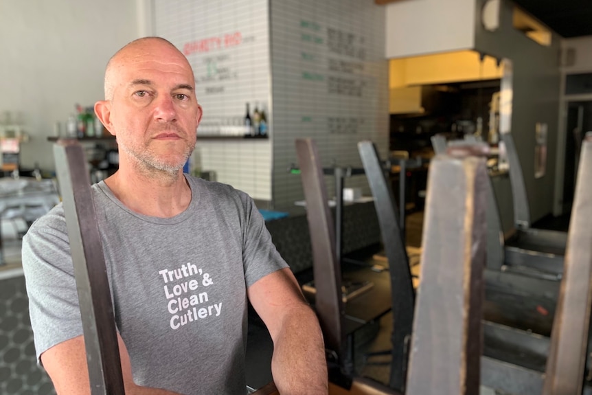 A man in a restaurant standing next to a table and chairs stacked up.