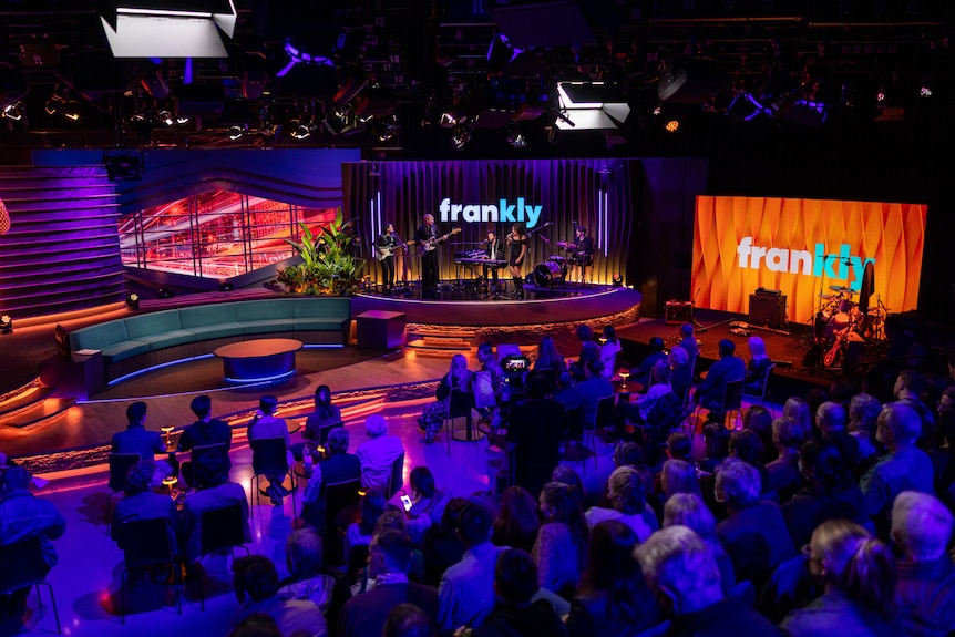 Wide show of TV studio showing band and audience.