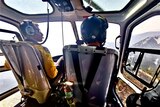 James Koens sits alongside another pilot in a helicopter flying over a bushfire.