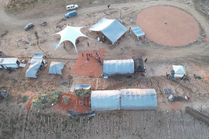 a bird's eye view of a cluster of tents on red coloured dirt