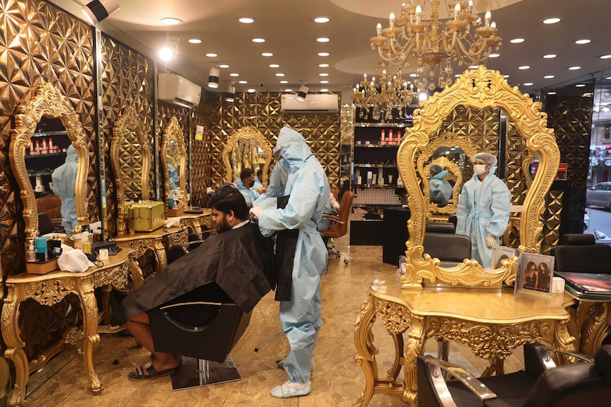 A hairdresser in personal protective suit attends to a customer at a hair salon in New Delhi, India.