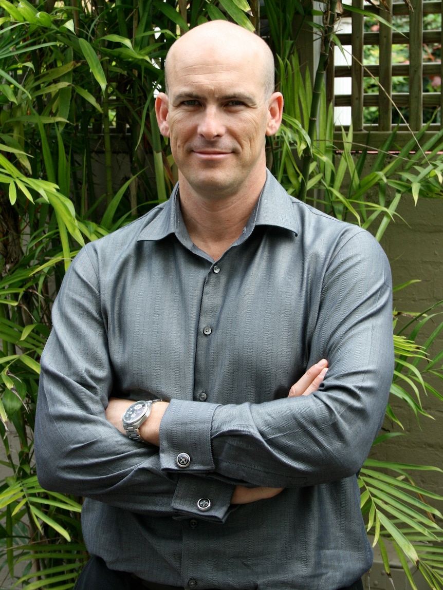 Gavin stands in front of a garden with his arms crossed