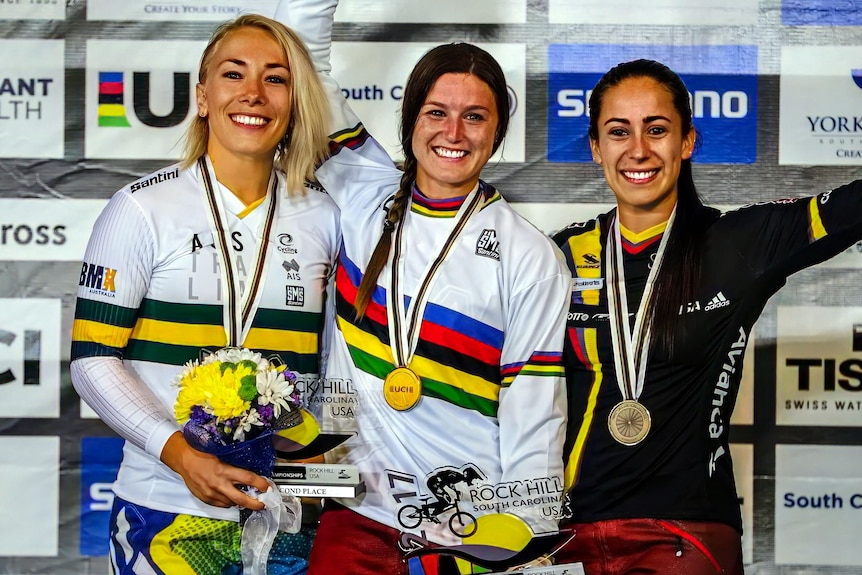 Alise Post smiles and waves on the podium wearing a rainbow jersey