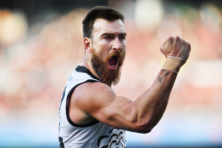 A Port Adelaide AFL player yells out as he pumps his right fist while celebrating a goal against Hawthorn.