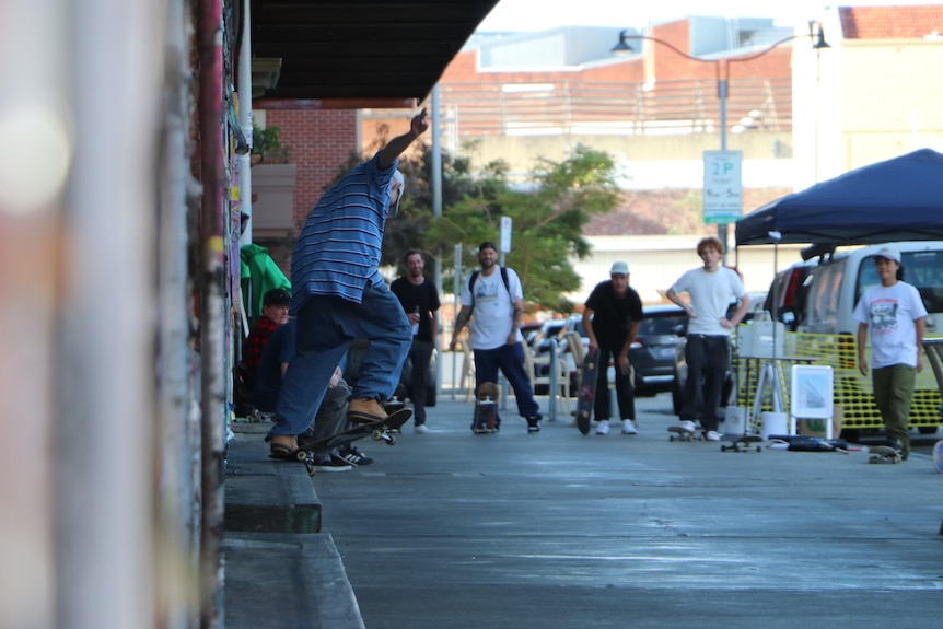 A man named Ben Bowring skates on a rail while being watched by other skaters. 