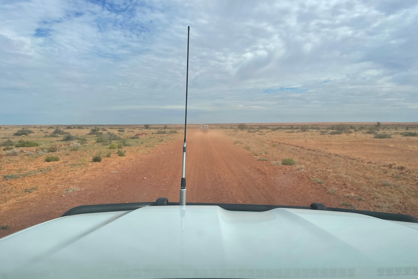 The view out a windscreen shows vast red dirt and a cloudy sky in Channel Country