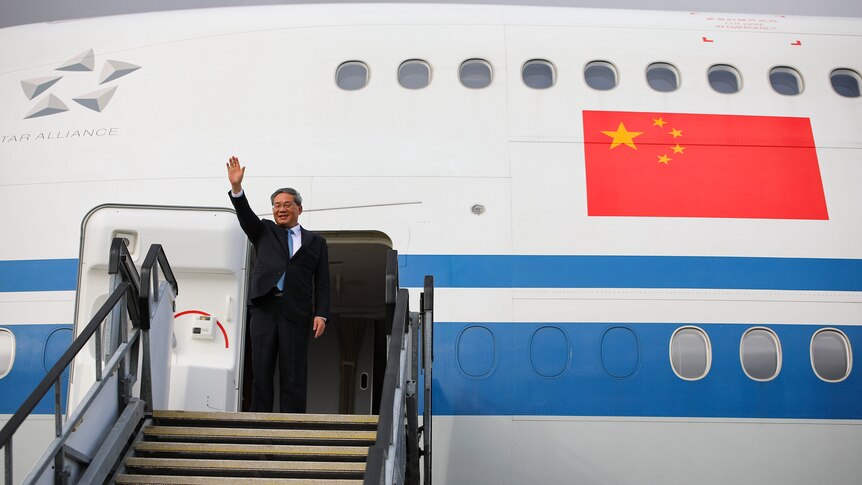 A man in a suit named Li Qiang waves before boarding a plane.