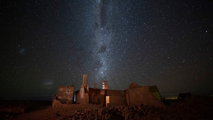 A stone building stands on rocky ground under the stars and Milky Way.