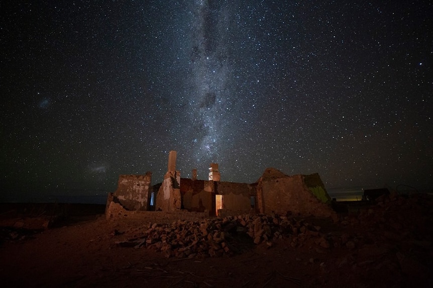 A stone building stands on rocky ground under the stars and Milky Way.